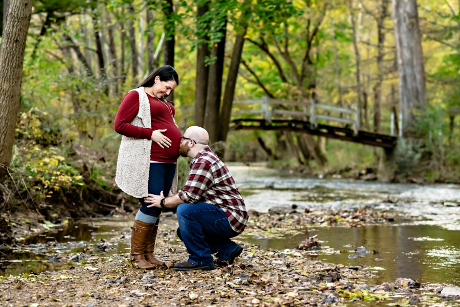 A father to be kisses the belly of his pregnant wife in valley forge state park.